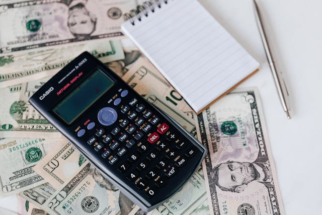 calculator and note pad on top of dollar bills 