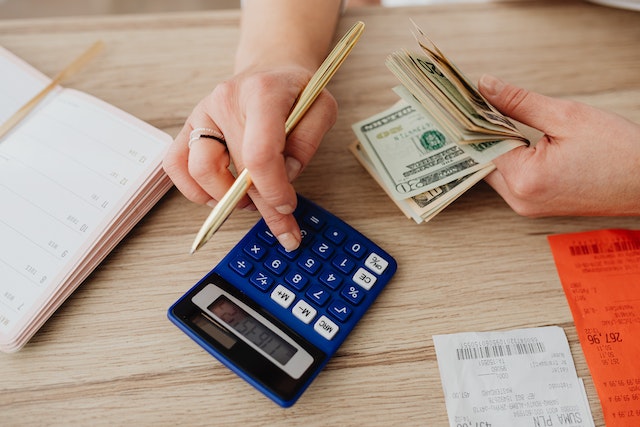 person holding money and typing on calculator